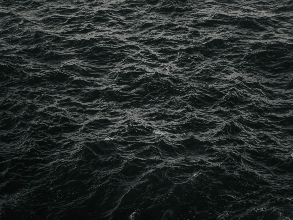 Monochrome wallpaper of dark water with rolling waves and gentle ripples creating texture