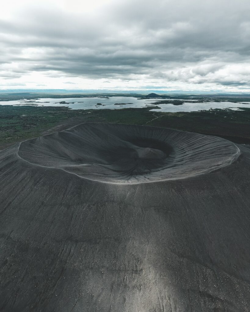 Monochrome volcanic crater wallpaper with rugged terrain dramatic clouds and distant serene lakes