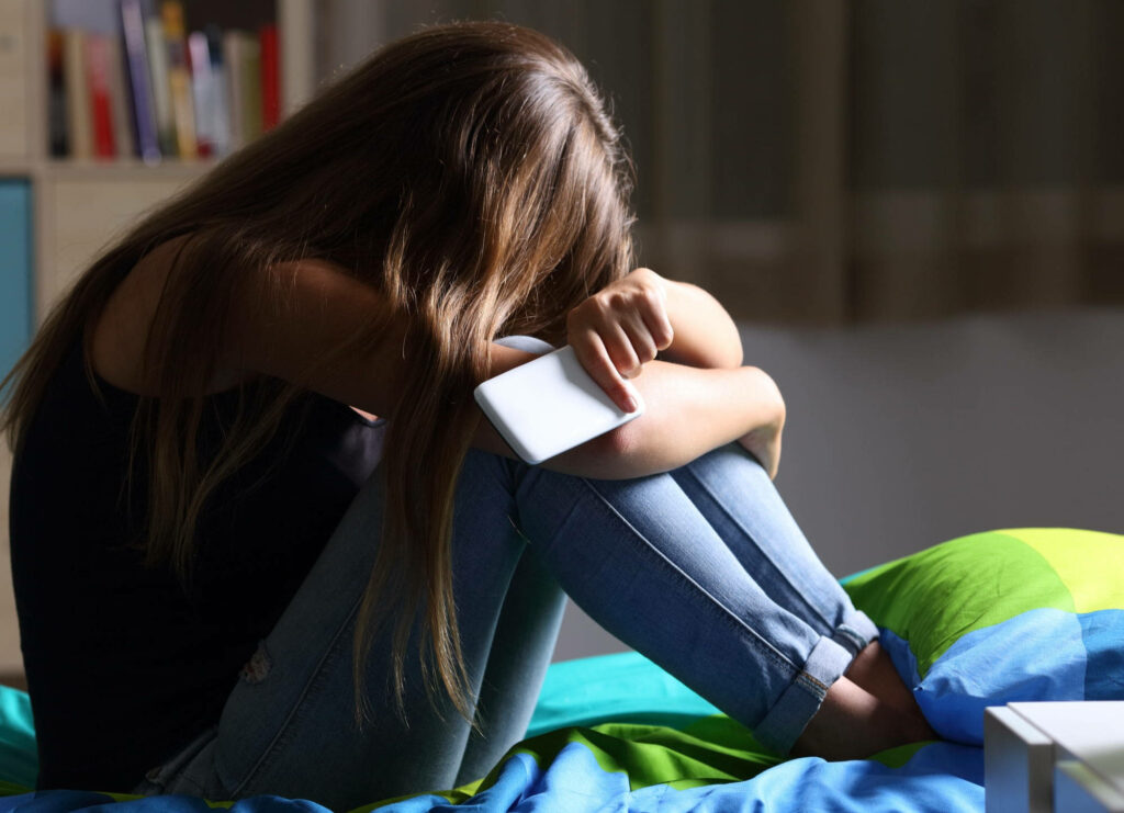 Solitude Reflected: An Emotive Shot of a Despondent Girl Seeking Solace in Her Bed Wallpaper