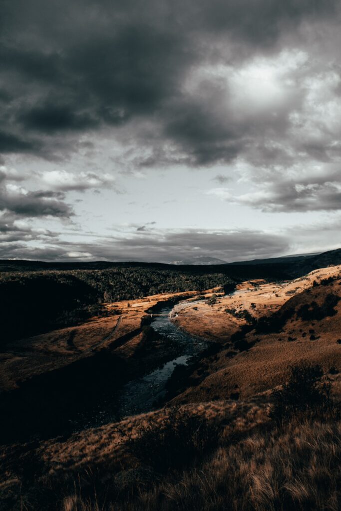 Aerial view of winding river through rugged landscape under dramatic cloudy skies wallpaper background