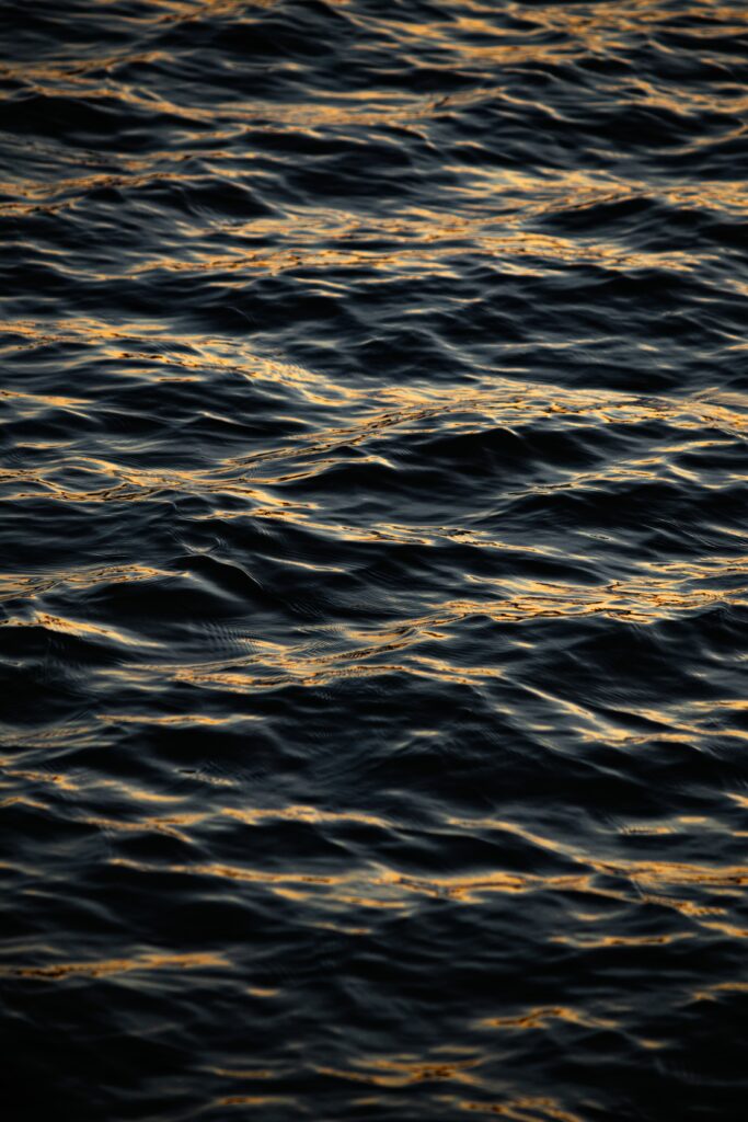 Moody black water wallpaper with gentle waves and golden light reflections creating calm ripples