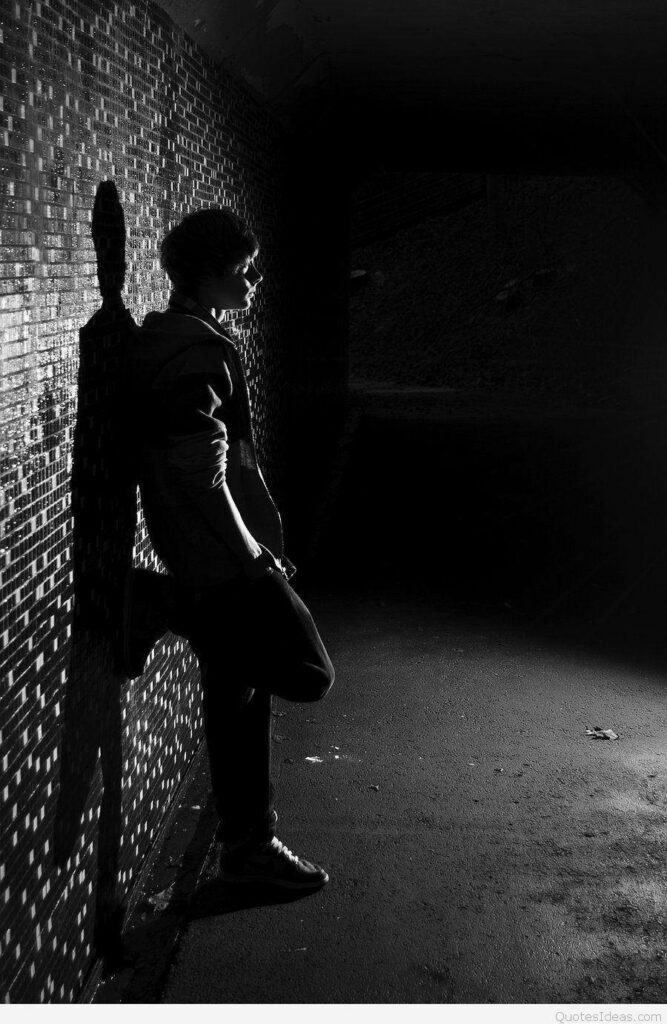 Solitary figure in black and white emo style against moody dimly lit tiled wall background Wallpaper