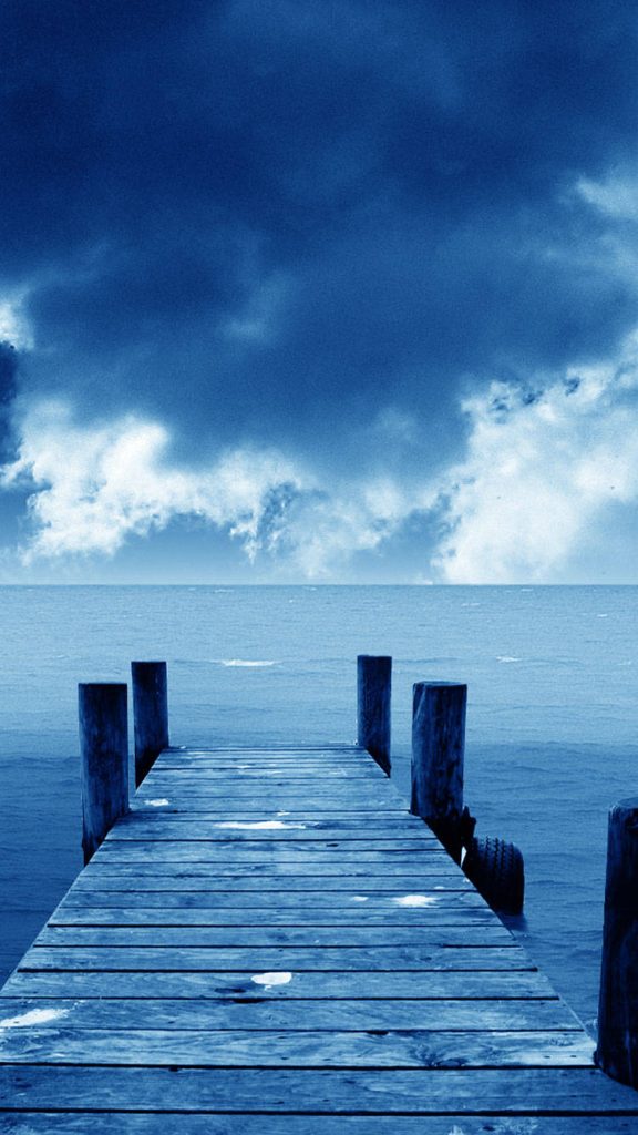 Serene blue iPhone wallpaper with weathered dock over calm deep blue water and cloudy sky