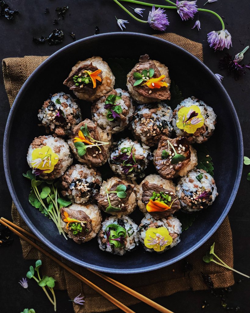Top-down moody photo of Bulgogi rice balls in dark bowl with sesame seeds edible flowers and microgreens Wallpaper