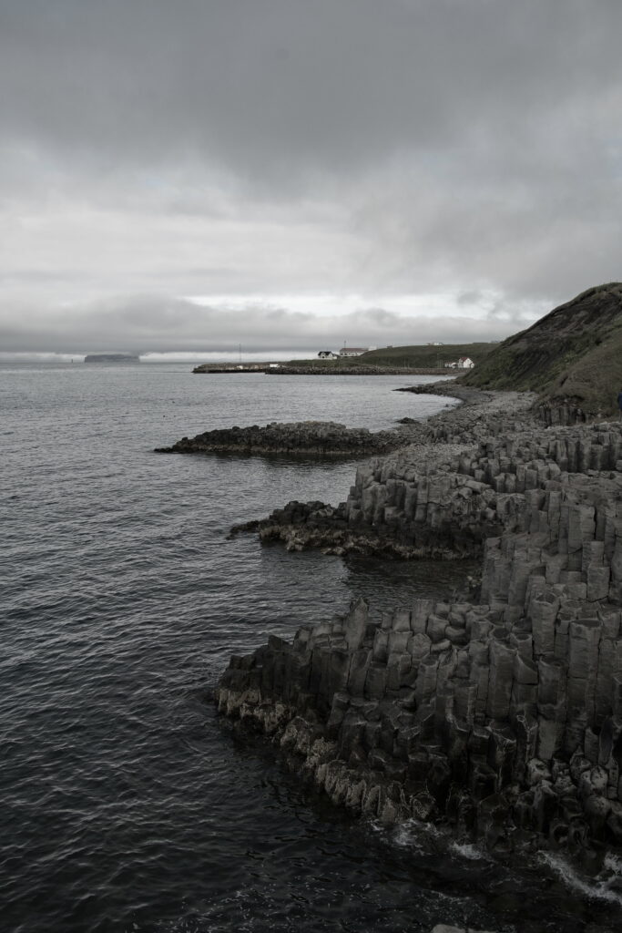 Moody coastal wallpaper with jagged basalt rocks and dark waves under overcast skies background