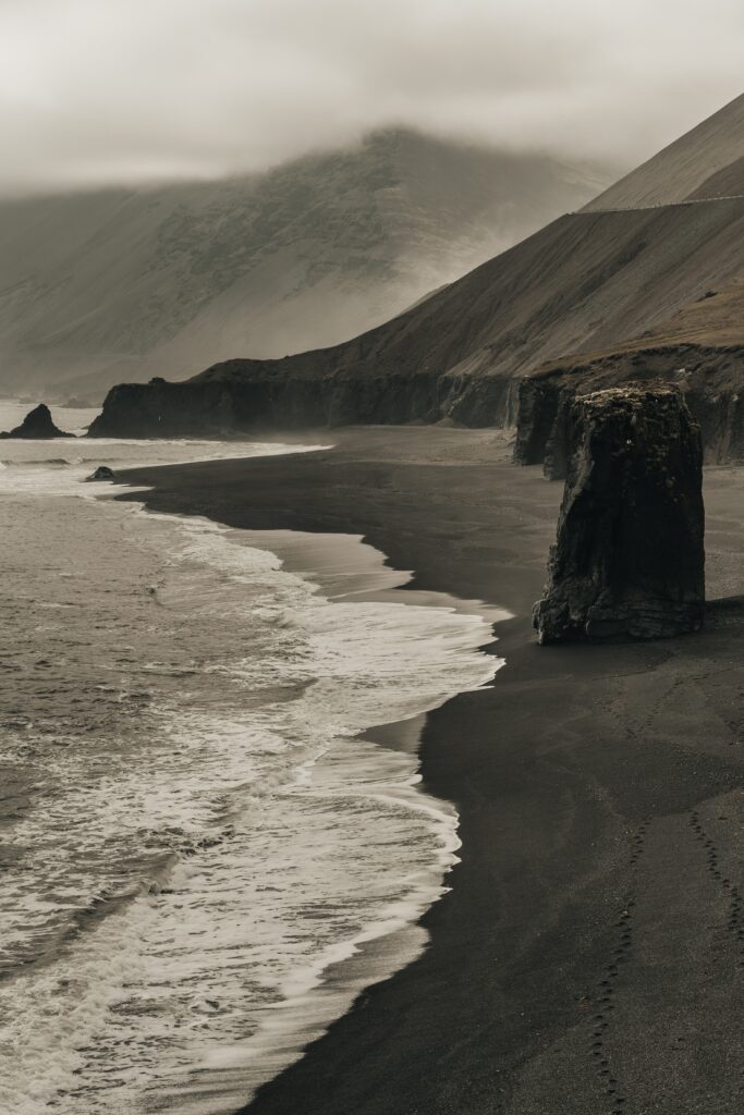 Moody beach scene with powerful waves dark sand rugged rocks foggy mountains tranquil seascape wallpaper