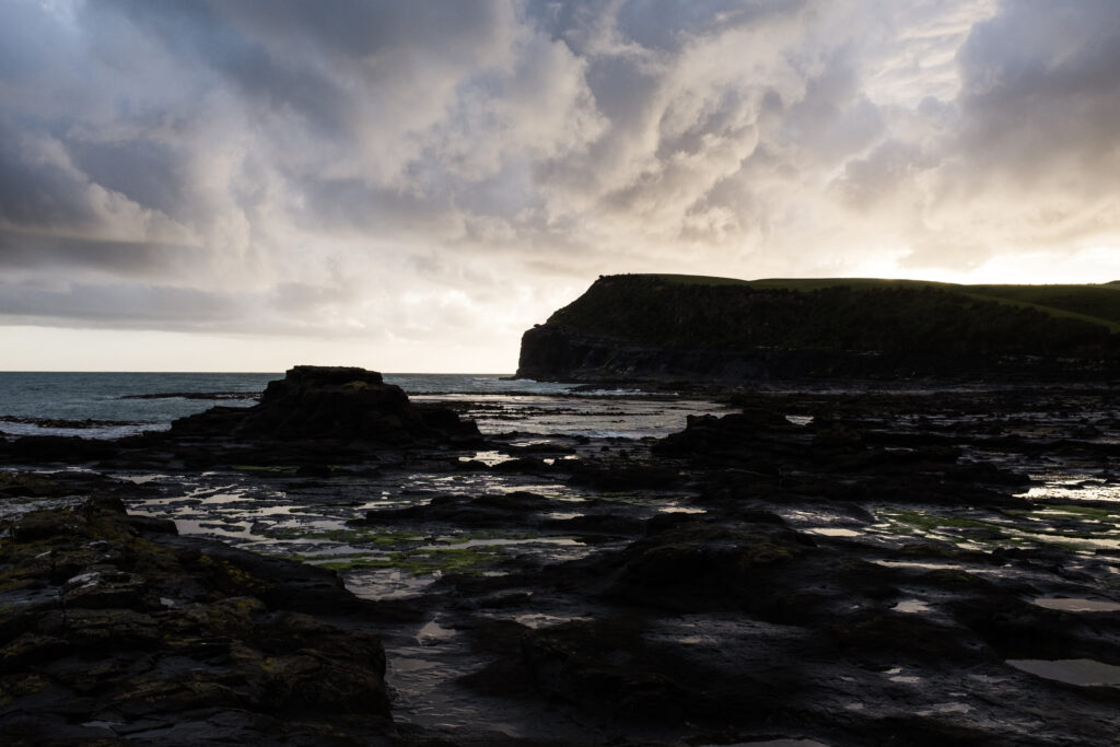 Dramatic coastal landscape with dark rocks tidal water and moody cloudy sky wallpaper background