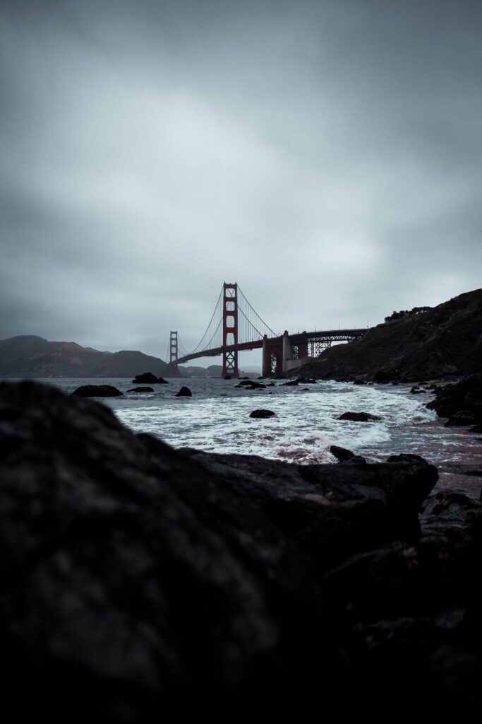Dramatic coastal scene with rugged rocks waves crashing bridge over misty sea moody sky wallpaper