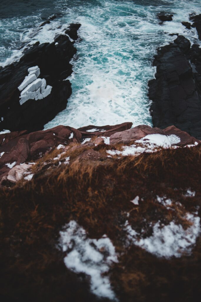 Dramatic coastal wallpaper with rugged rocks foaming waves snow patches and dry grass foreground