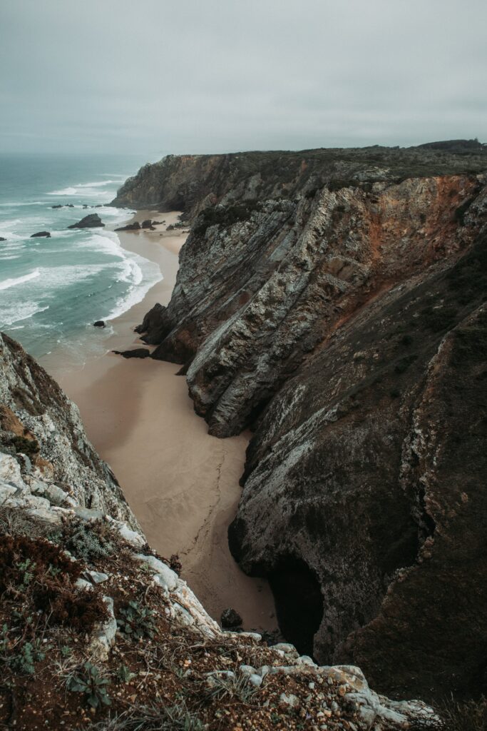 Dramatic coastline with towering cliffs secluded sandy beach rolling waves moody skies wallpaper