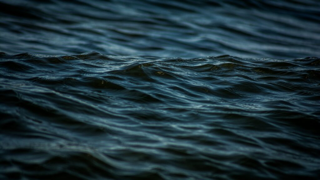 Moody dark blue and black water surface with gentle waves and ripples wallpaper background