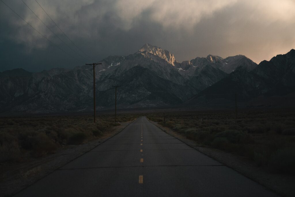 Desolate road with yellow lines leading to rugged mountains under dark moody clouds wallpaper
