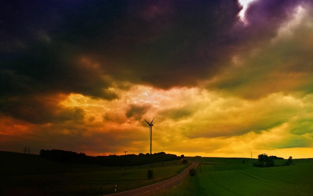 Dramatic dark clouds over green meadows and windmill at moody evening storm wallpaper background