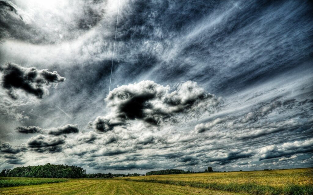 Dramatic gray swirling clouds over vast field moody landscape earth tones wallpaper background