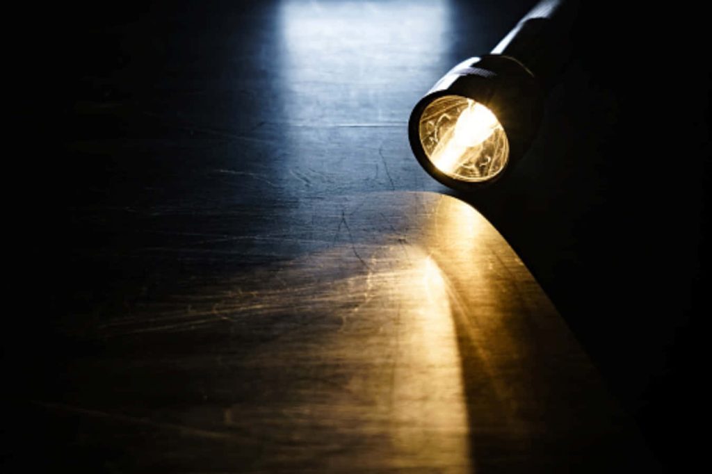 Handheld flashlight casting warm beam on dark textured surface moody wallpaper background