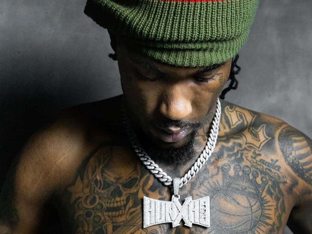 Close-up portrait of rapper Hunxho with diamond pendant green beanie and detailed chest tattoos Wallpaper