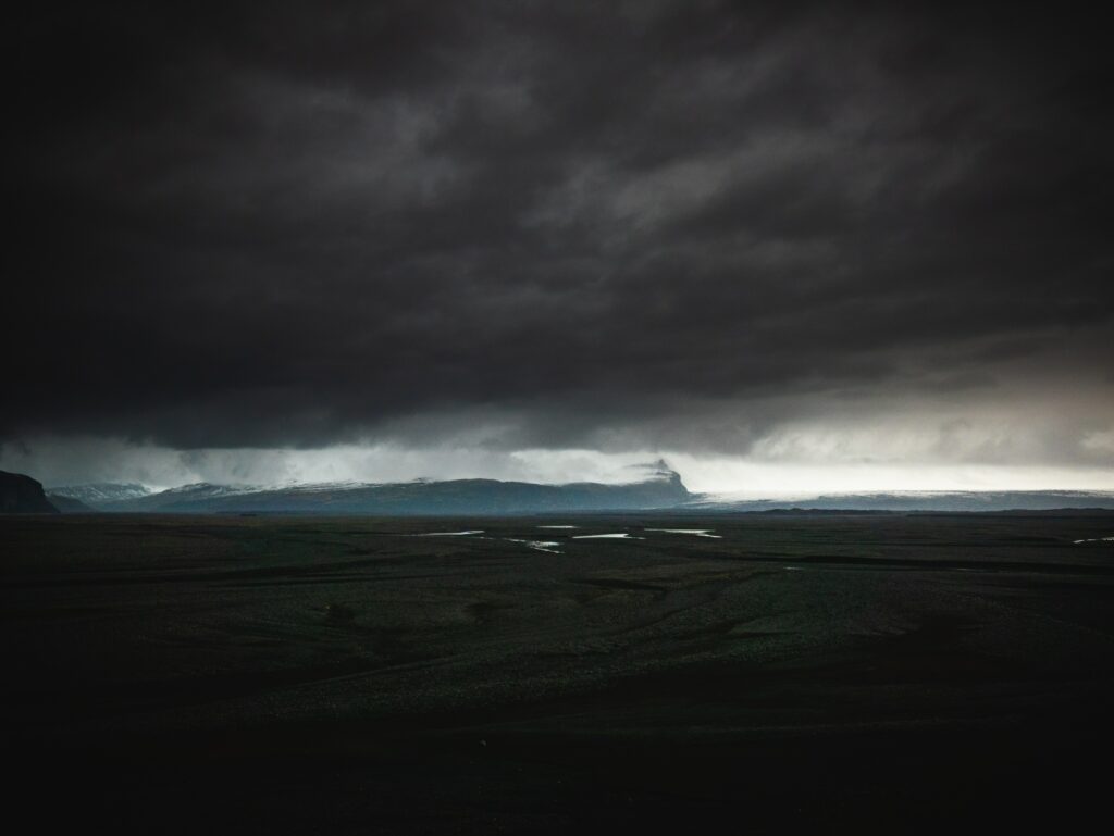 Brooding dark sky with dense clouds over desolate Icelandic landscape and reflective water pools Wallpaper