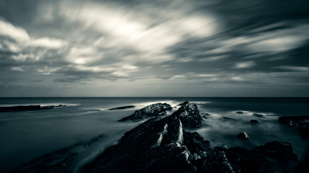 Dramatic seascape with jagged rocks misty water moody overcast sky dark monochrome wallpaper