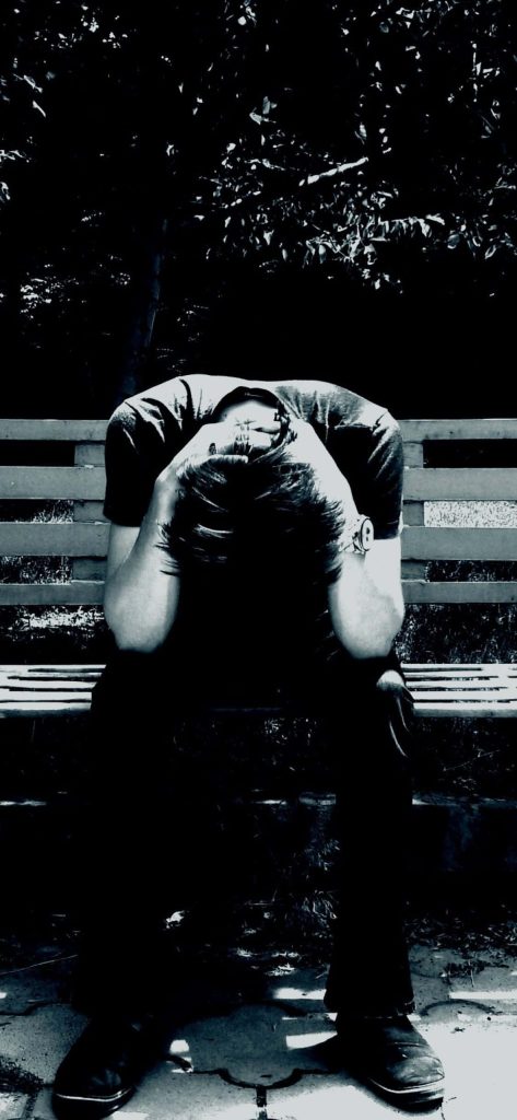 High contrast black and white wallpaper of distressed man sitting on bench with head in hands