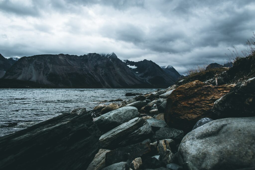 Moody mountain landscape with rugged rocks foggy peaks lake shore overcast sky wallpaper