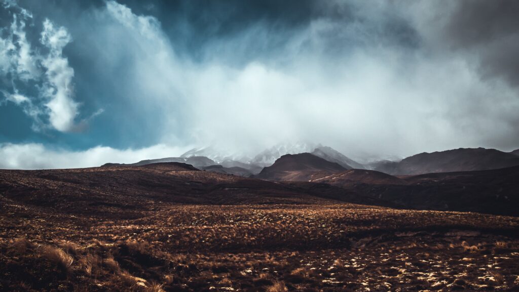 Dramatic foggy mountain landscape with moody blue sky and rich earthy foreground tones wallpaper
