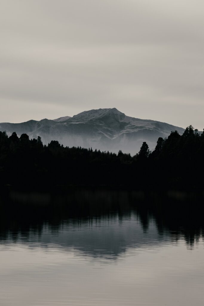 Moody mountain landscape with dark forest and lake reflection under cloudy overcast sky wallpaper