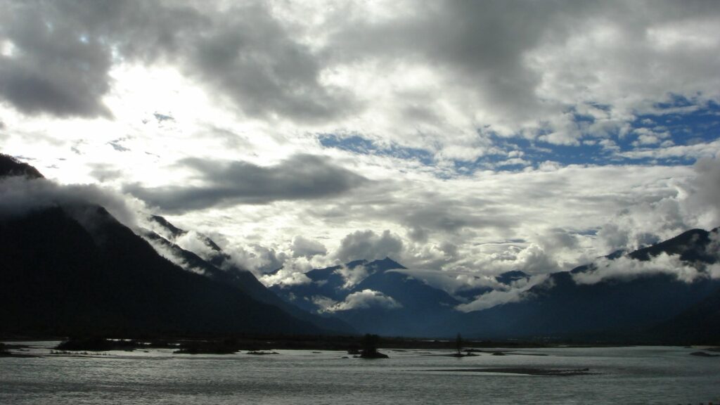 Dramatic moody landscape with heavy clouds rugged mountains misty peaks calm water wallpaper