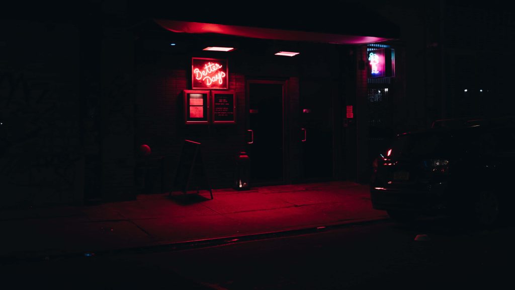Moody night scene with car outside Better Days neon sign glowing in dark urban street setting Wallpaper