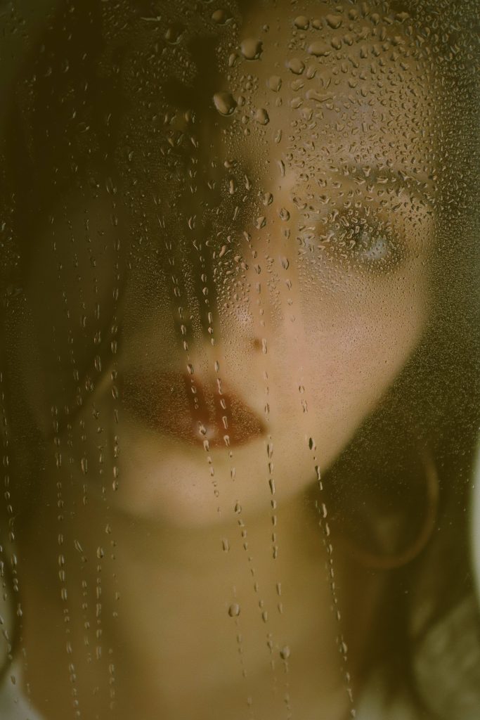 Close-up portrait of a woman with red lips behind rain-covered glass warm moody mobile wallpaper
