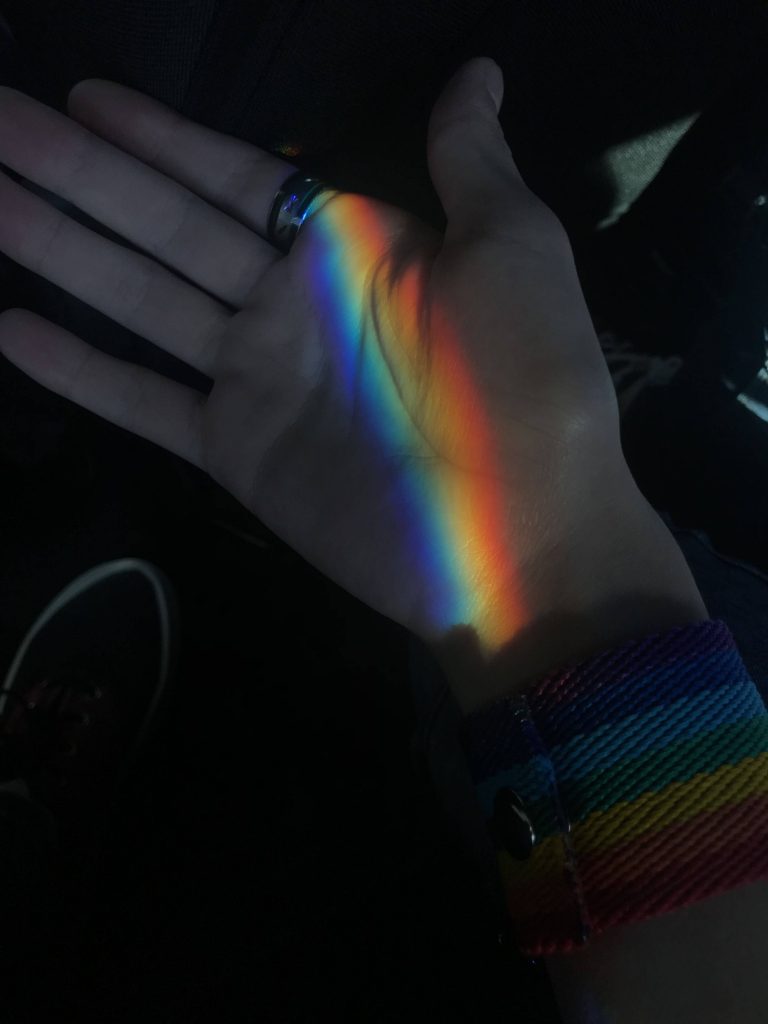 Open palm lit by vibrant rainbow light with striped wristband and ring on dark background wallpaper