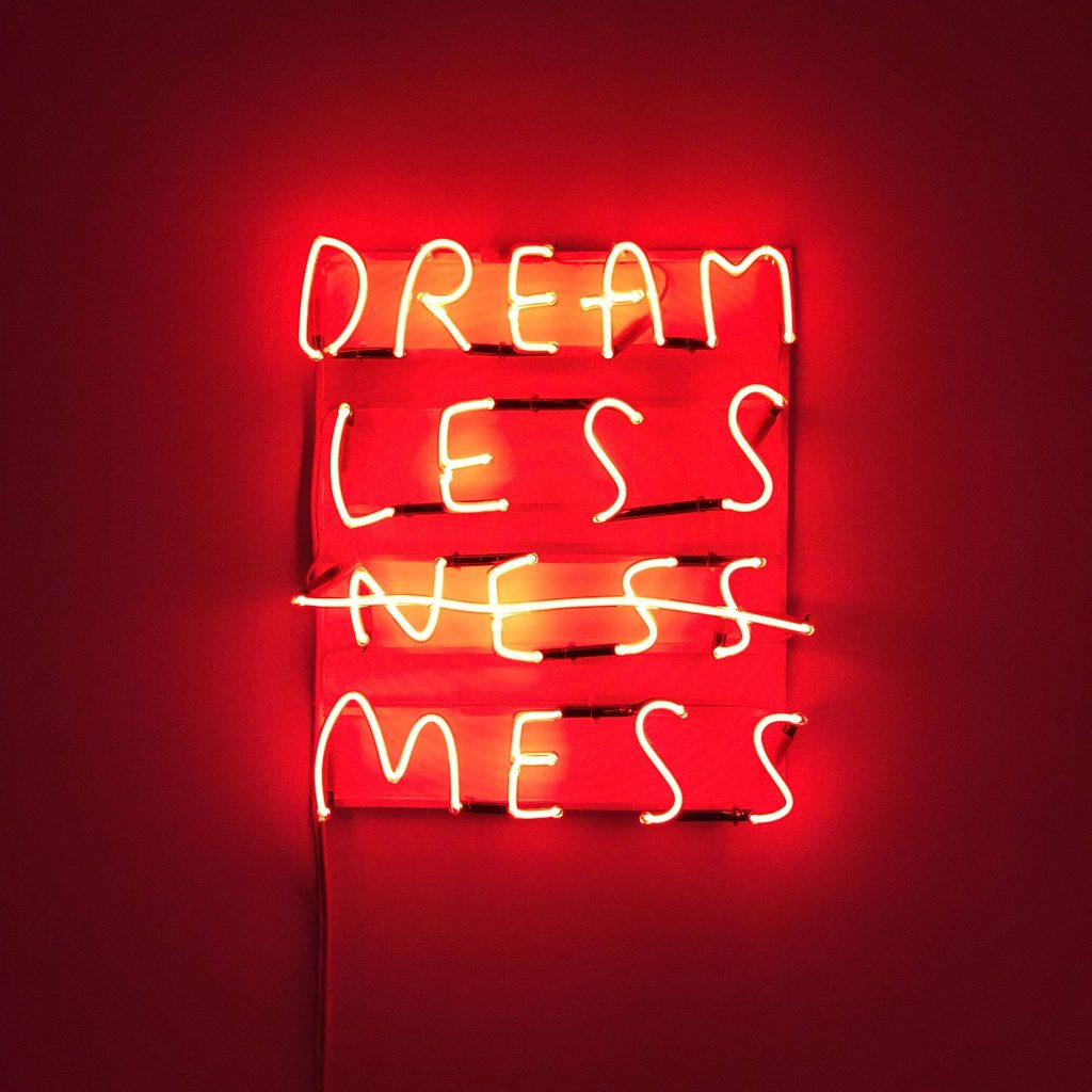 Moody red neon sign reading DREAM LESS NESS MESS on dark crimson minimalist wallpaper background