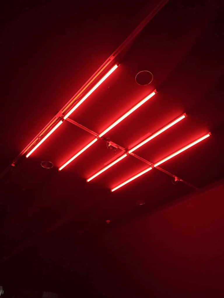 Moody desktop wallpaper with vibrant red neon linear lights on a dark minimal ceiling background