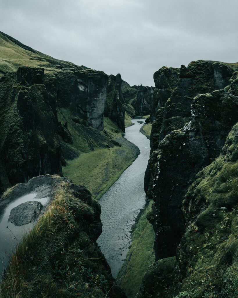 Winding river flowing through dramatic cliffs mossy rocks and lush green grass under overcast sky Wallpaper