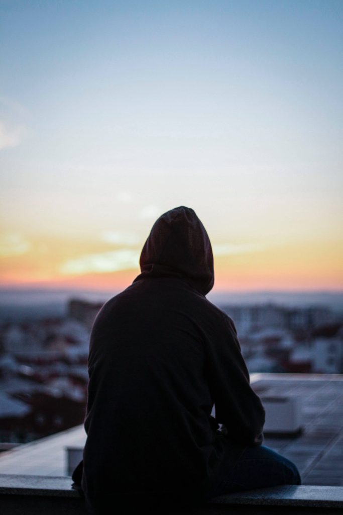 Lone man in hoodie on rooftop at dusk with cinematic lighting and blurred city background Wallpaper