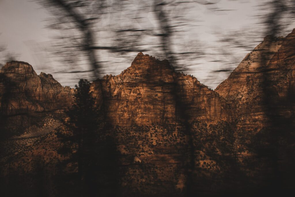 Rugged brown mountains with rocky formations and blurred tree silhouettes in moody landscape Wallpaper