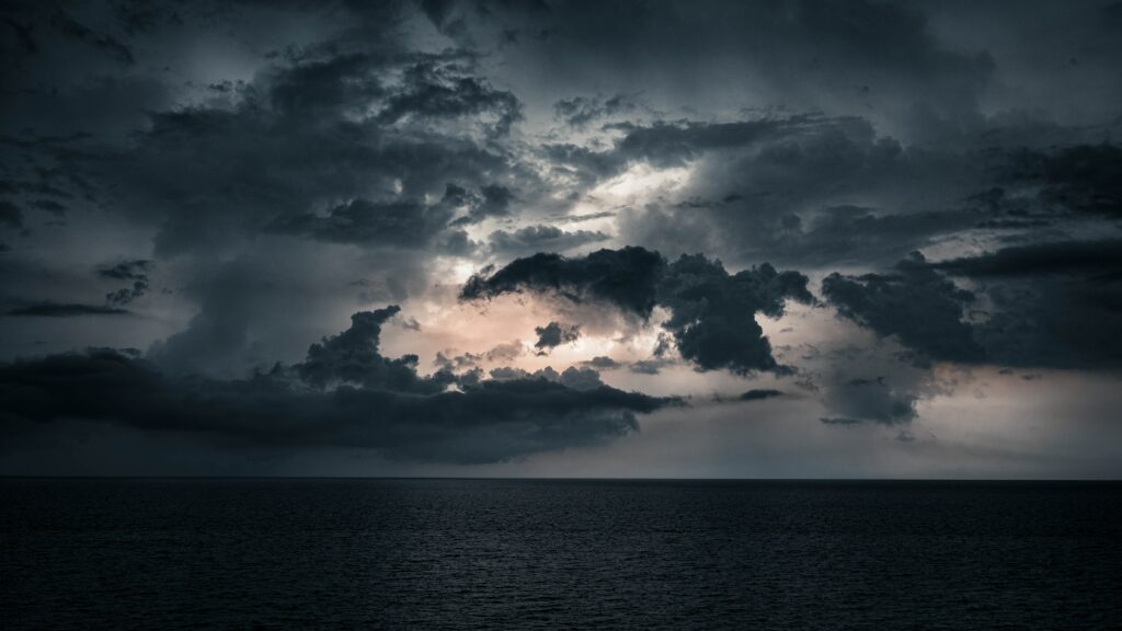 Dramatic moody seascape wallpaper with deep blue sea and brooding dusk sky clouds background