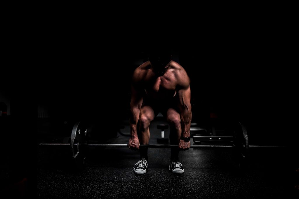 Muscular man lifting heavy barbell in dim gym with dramatic lighting strength training wallpaper