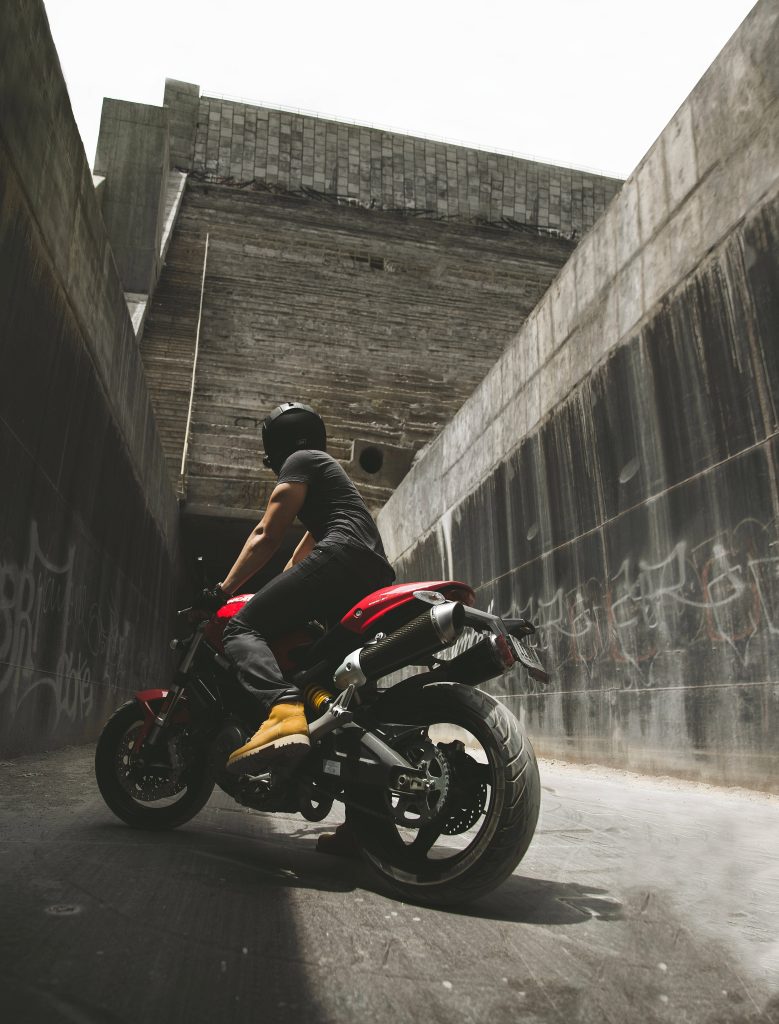 Motorcyclist on red Ducati riding through graffiti-covered narrow urban concrete passageway at dusk Wallpaper