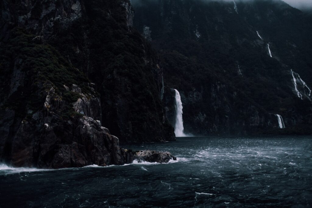 Moody waterfall cascading over rugged cliffs into turbulent sea with mist and dark rocks wallpaper