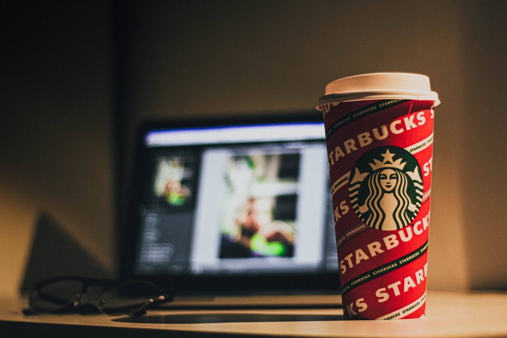 Moody workspace wallpaper with vibrant red Starbucks cup laptop photo editing and glasses