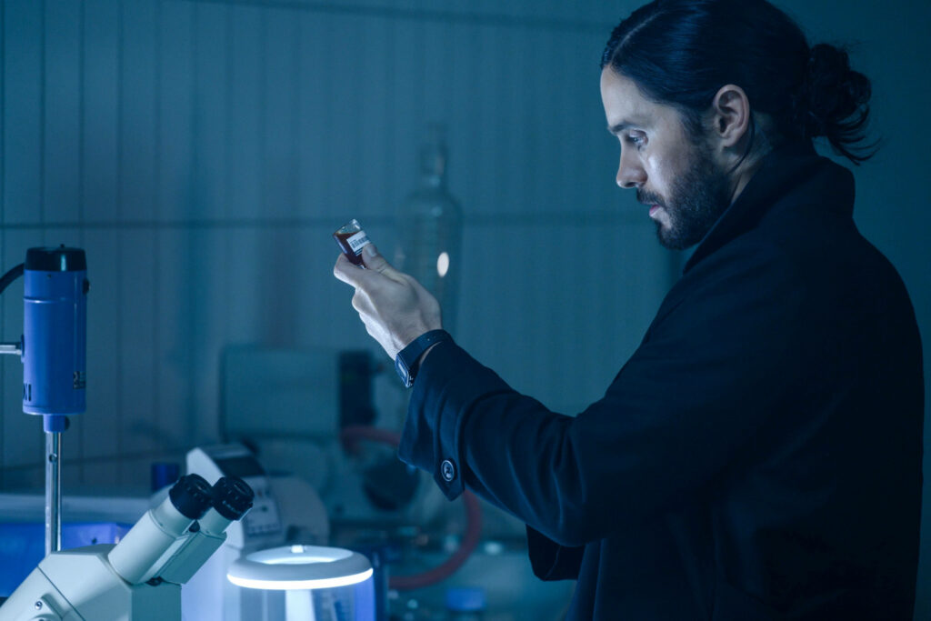 Morbius in blue-lit laboratory carefully examining vial with scientific equipment background wallpaper