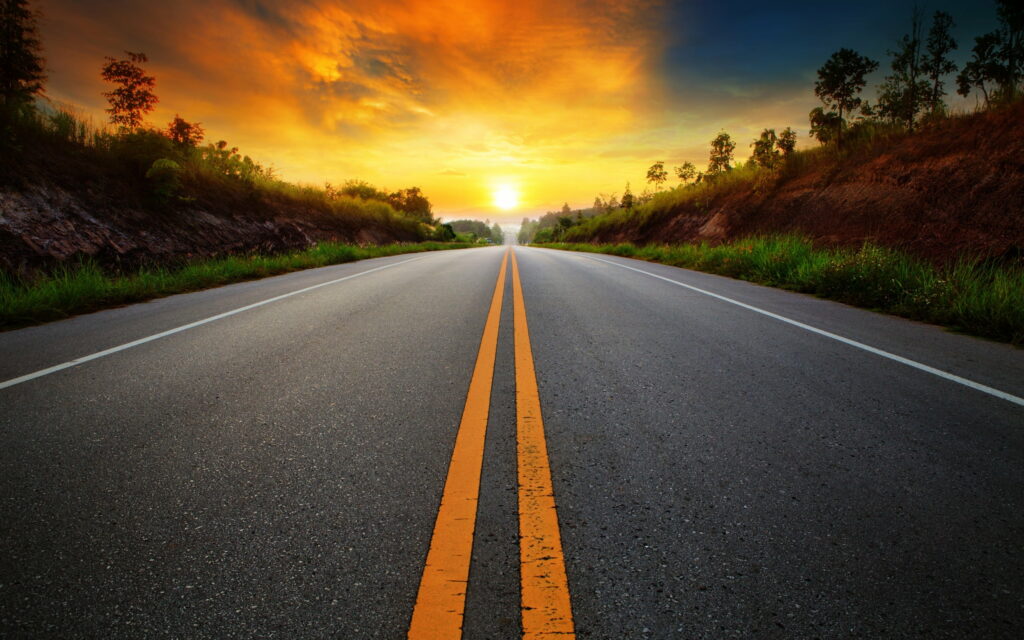Scenic highway at sunrise with golden sky and grassy embankments QHD desktop wallpaper background