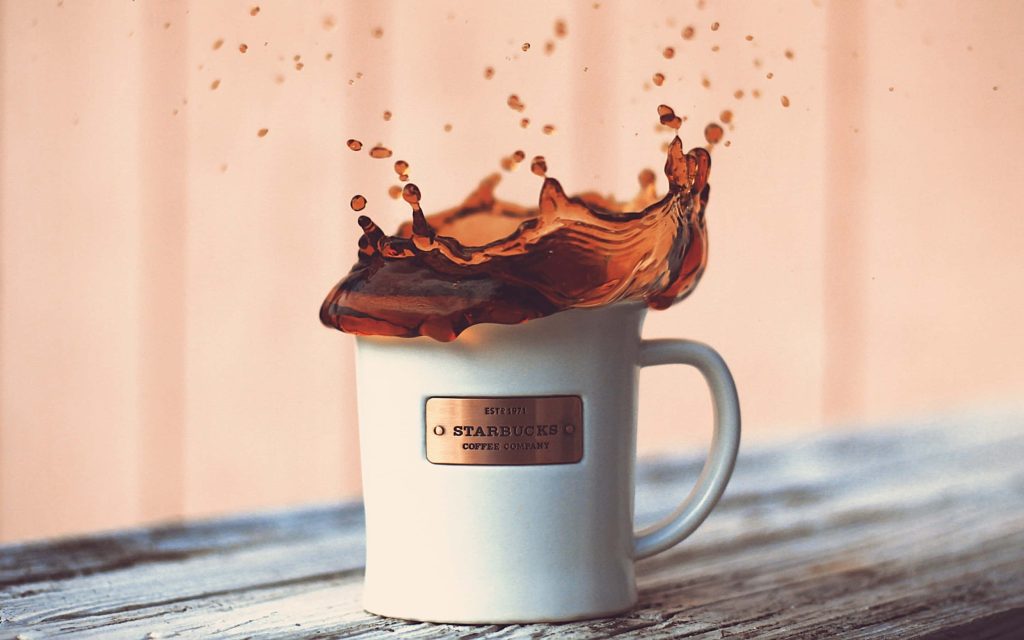 White Starbucks coffee mug splashing dark coffee on rustic wood with soft peach background wallpaper