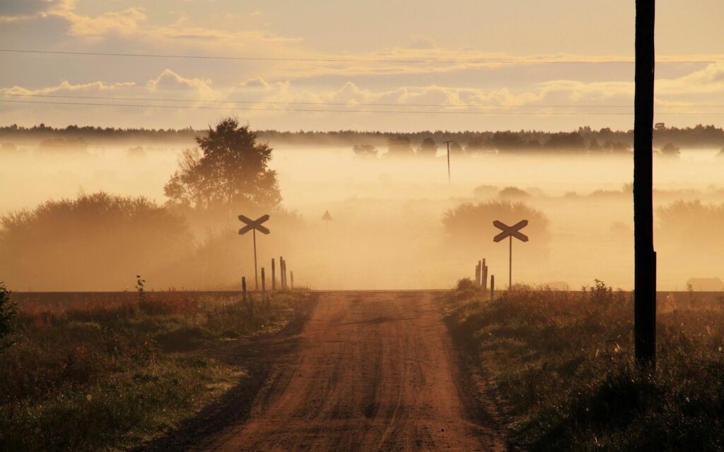 Foggy rural road at dawn with railroad crossing signs and soft morning light wallpaper background