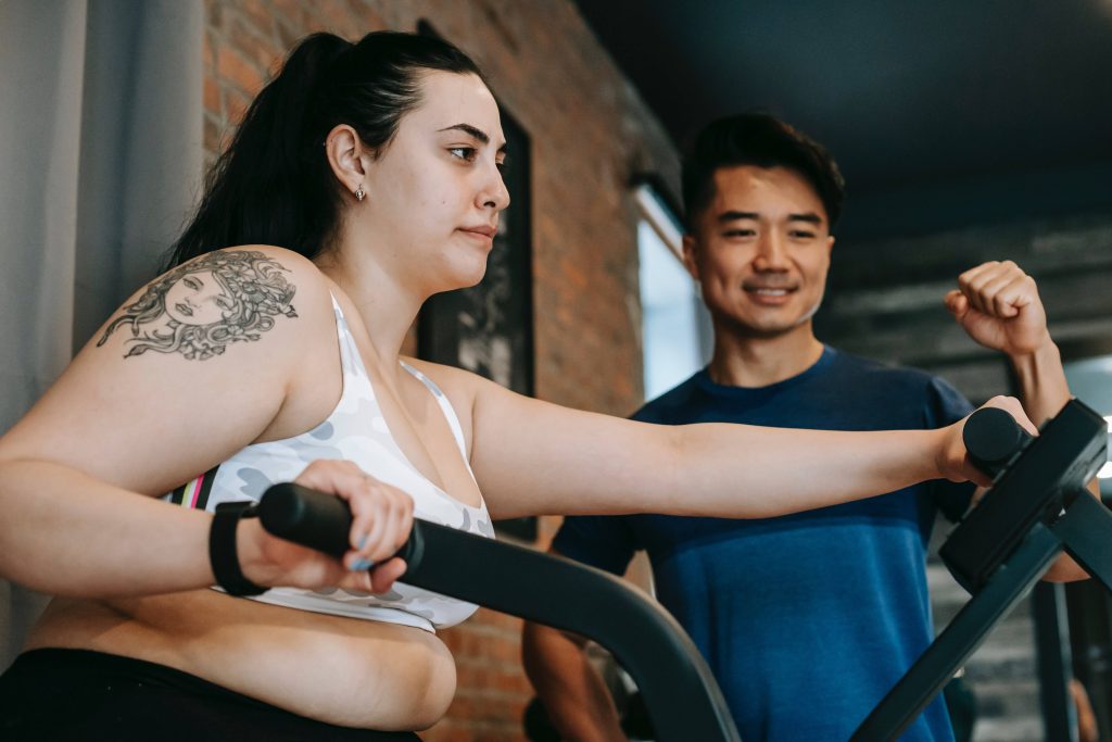 Motivated plus size woman exercises with personal trainer workout gym brick wall fitness motivation Wallpaper