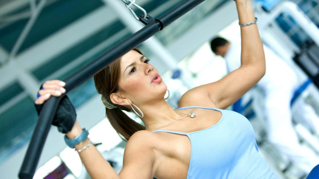 Focused woman in blue tank top doing lat pulldown exercise in bright gym setting wallpaper