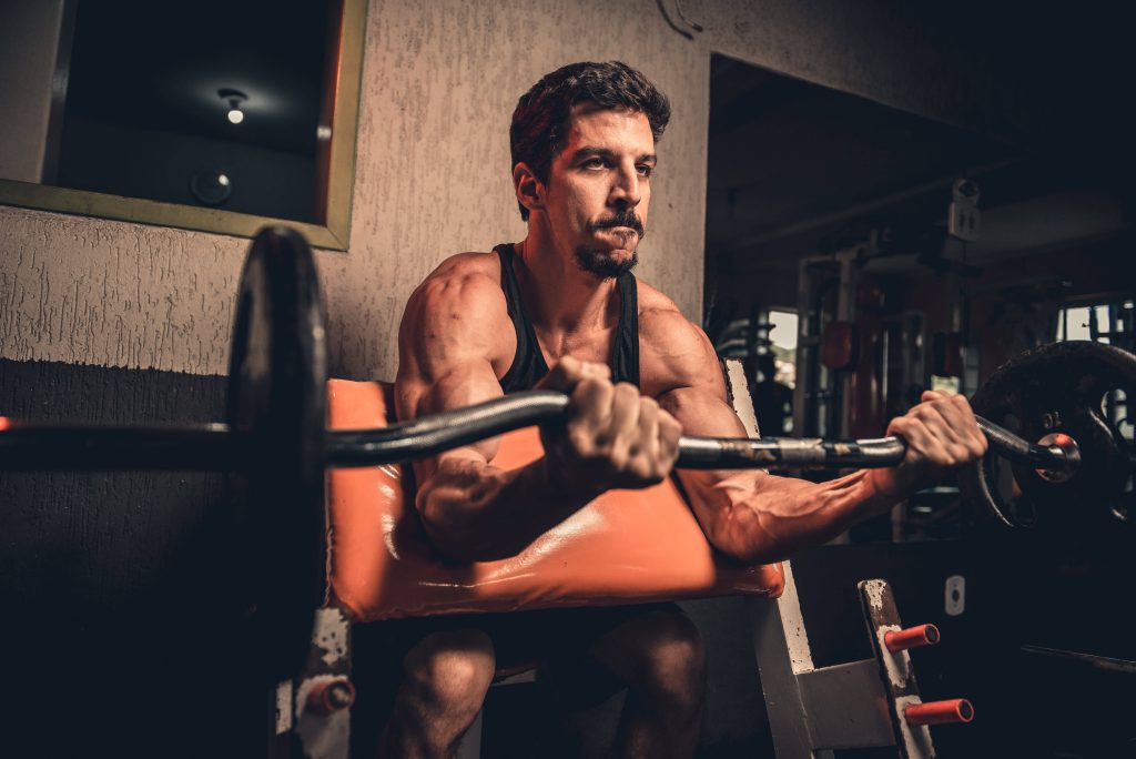 Muscular man doing bicep curls with EZ bar on preacher bench in moody gym setting wallpaper