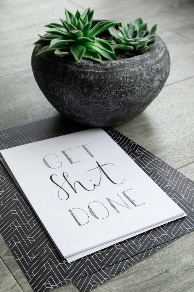 High-angle view of succulent in concrete pot with handwritten get shit done quote on grid paper Wallpaper
