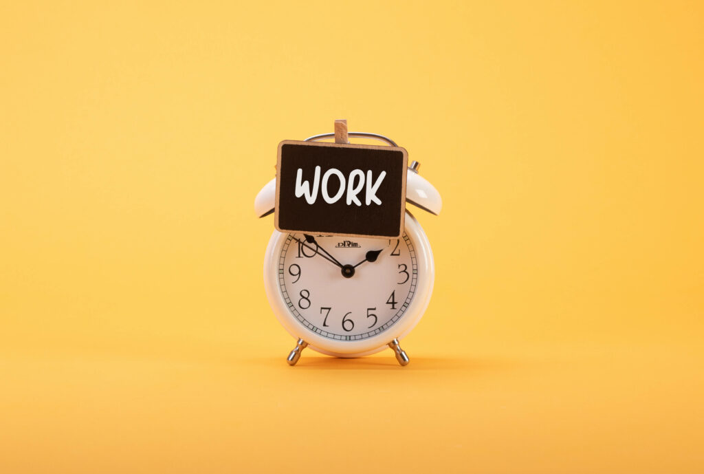 White classic alarm clock with WORK sign on blackboard yellow background productivity wallpaper