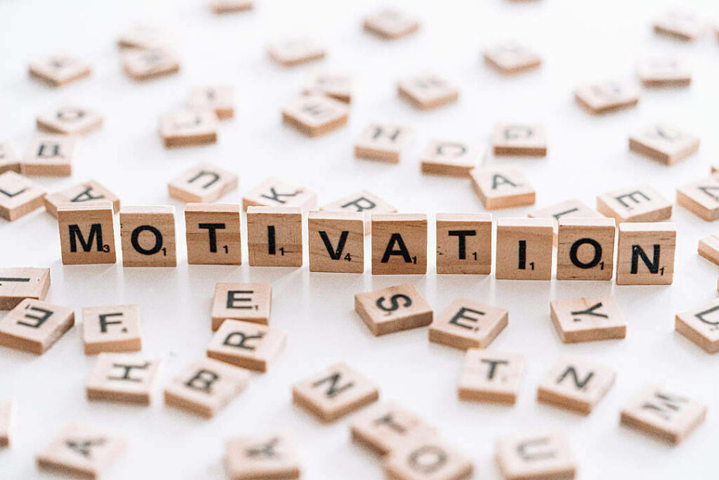 Motivation spelled out with brown Scrabble tiles amidst scattered tiles on white table, setting a backdrop for inspiring quotes Wallpaper